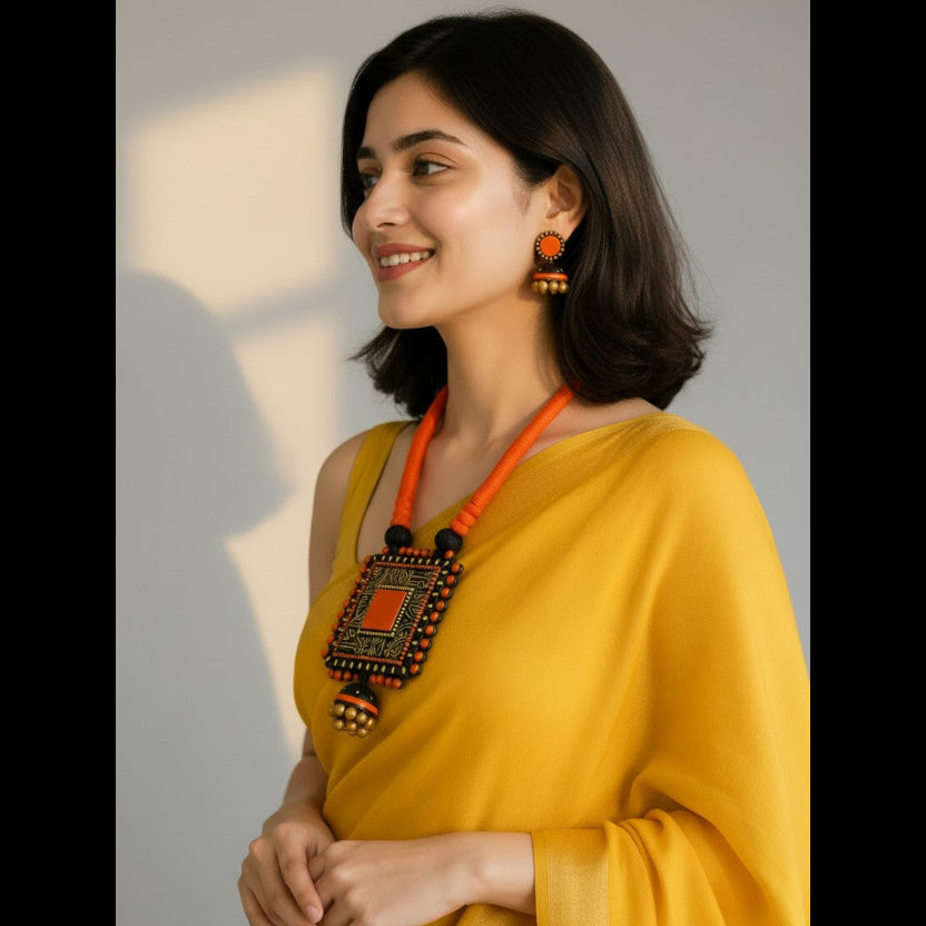 A woman wearing a bright yellow draped garment and a bold orange and black geometric statement necklace, photographed against a soft light gray background with warm sunlight and shadows.