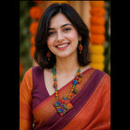 A woman smiling and wearing a traditional Indian sari with a deep purple body, orange sleeves, and a rust-orange border, accessorized with a colorful beaded necklace and earrings.