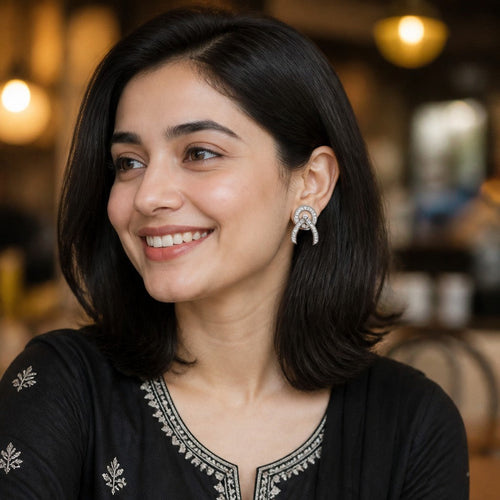 A woman with dark shoulder-length hair smiling and looking to the side, wearing a black embroidered kurta with silver-toned detailing on the neckline and sleeves, set against a softly blurred cafe background.