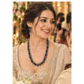 A woman wearing a traditional Indian outfit with a beaded necklace and matching earrings, smiling in a decorated event setting.