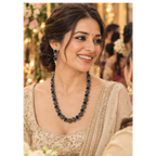 A woman wearing a traditional Indian outfit with a beaded necklace and matching earrings, smiling in a decorated event setting.