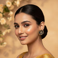 A woman with dark hair styled in a low bun wears a golden yellow saree with subtle embroidered details and a matching blouse. She is wearing a decorative gold and black statement earring.