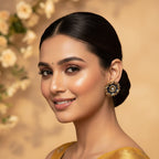 A woman with dark hair styled in a low bun wears a golden yellow saree with subtle embroidered details and a matching blouse. She is wearing a decorative gold and black statement earring.