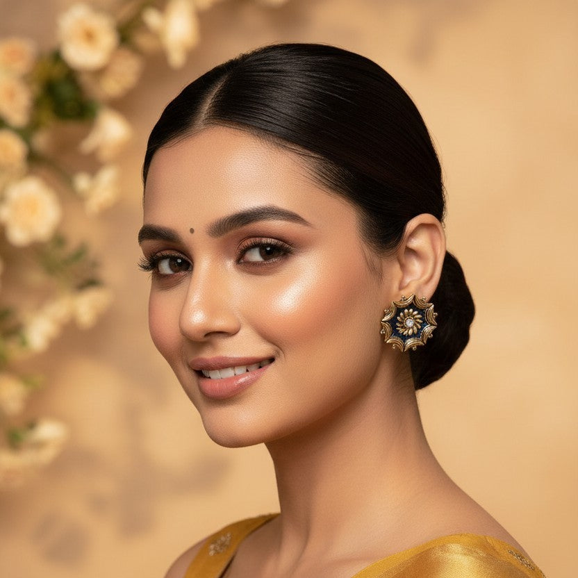 A woman with dark hair styled in a low bun wears a golden yellow saree with subtle embroidered details and a matching blouse. She is wearing a decorative gold and black statement earring.