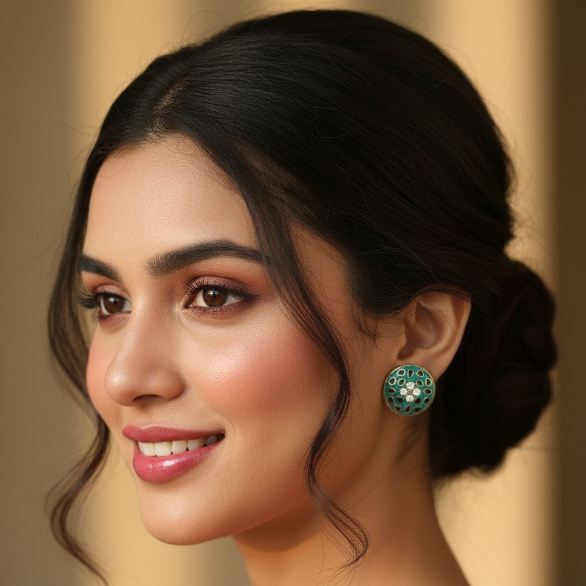 A woman in a red traditional outfit with gold embroidery is shown in a close-up portrait, wearing a green and silver stud earring against a soft beige background.