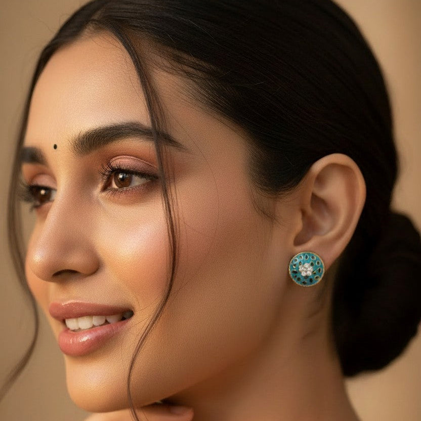 A close-up portrait of a woman wearing a round turquoise and white beaded earring, with her hand near her chin against a warm beige background.