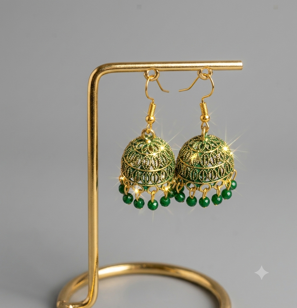 A pair of gold-toned filigree jhumka earrings with green bead fringe, displayed on a gold stand against a neutral gray background.