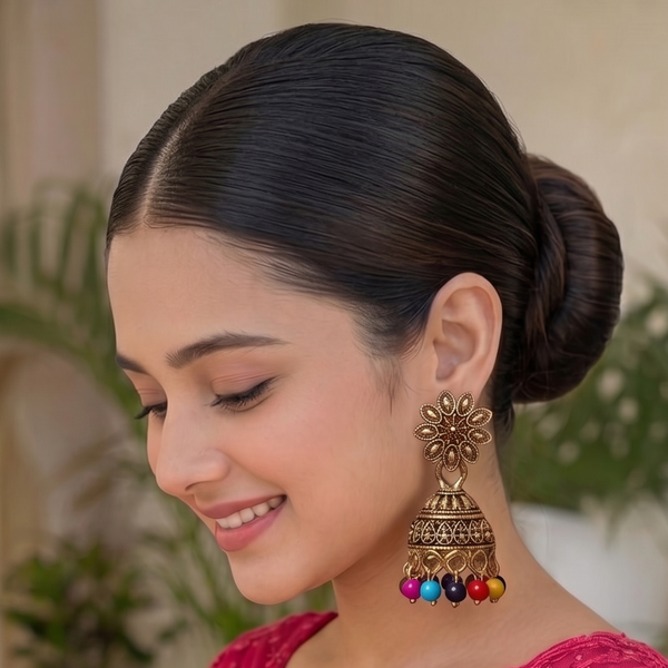 A woman wearing a bright pink embroidered traditional outfit with sheer lace sleeves and matching pink jewelry, photographed in a softly blurred indoor setting with plants in the background.