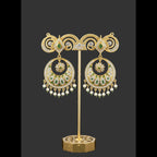A pair of gold-toned traditional Indian jhumka earrings with intricate filigree work, small green stone accents, and dangling pearl-like beads, shown on a plain light background.