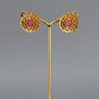 A pair of gold-toned floral mandala stud earrings with ruby-red stone centers, displayed on a plain background.