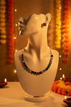 A silver-tone necklace and matching stud earrings set with round, colorful gemstone-like beads in red, green, pink, blue, black, and white, displayed on a light fabric background.