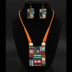 A colorful geometric jewelry set displayed on a white mannequin bust, featuring a square pendant necklace and matching rectangular earrings with a bold multicolor pattern and bright orange cords.