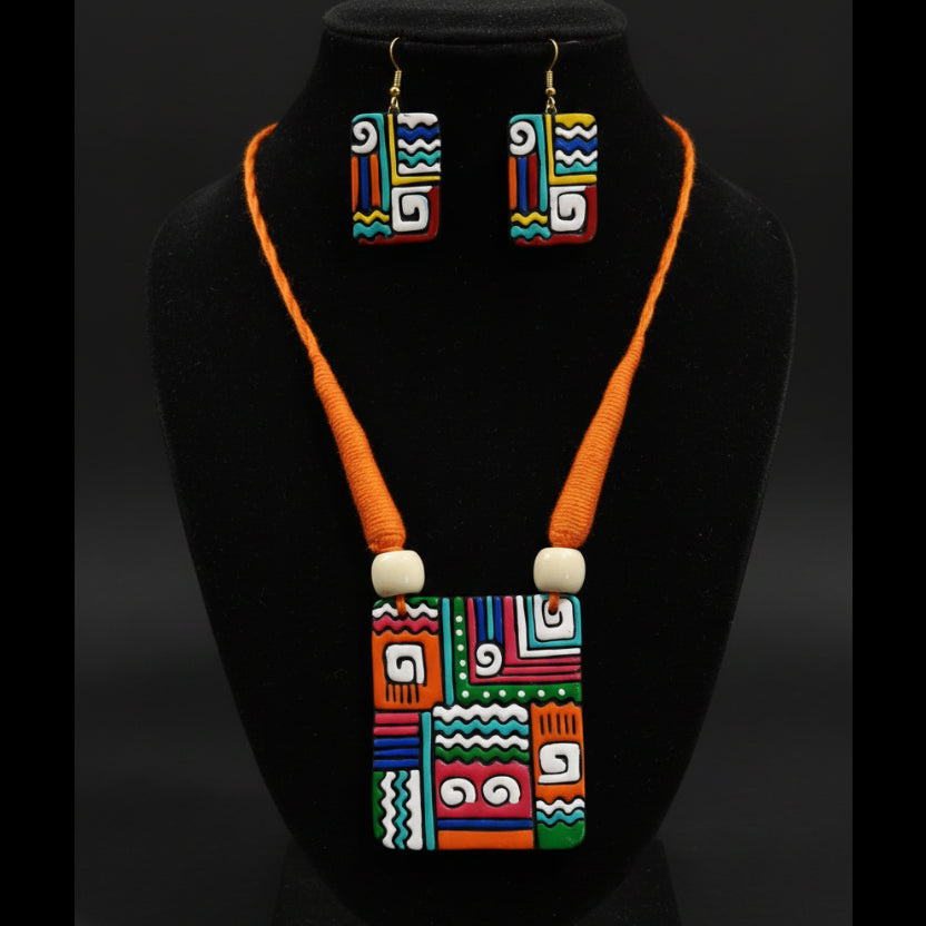 A colorful geometric jewelry set displayed on a white mannequin bust, featuring a square pendant necklace and matching rectangular earrings with a bold multicolor pattern and bright orange cords.