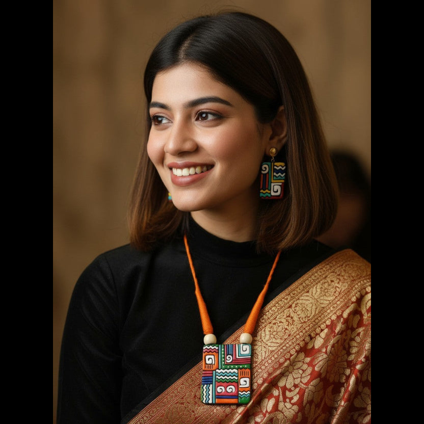 A woman with shoulder-length dark brown hair is shown in a close-up portrait, wearing a black top and a gold-patterned sari, with a colorful geometric pendant necklace and matching earrings.