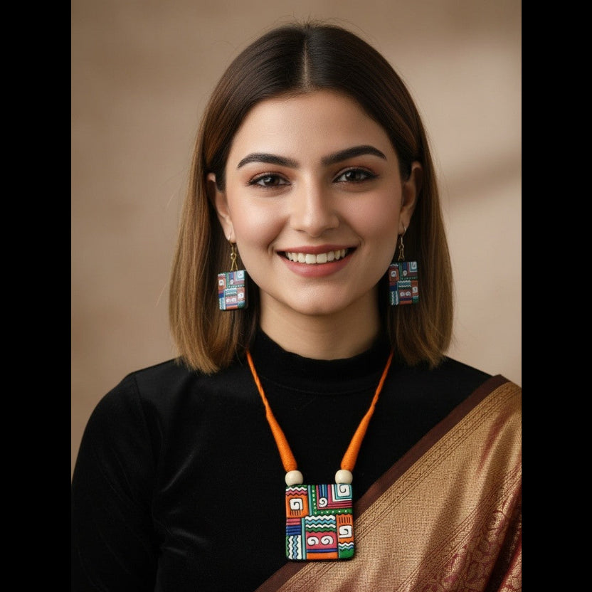 A smiling woman with shoulder-length brown hair is shown from the chest up against a warm beige studio background. She wears a black top and a bronze-brown sari, with a colorful geometric pendant necklace and matching earrings.