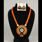 A traditional Indian jewelry set featuring a necklace and matching earrings displayed on a white mannequin bust. The jewelry has vibrant orange cords, blue and gold painted jhumka-style pendants, and orange bead details.