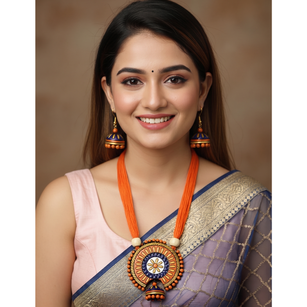 A smiling woman wearing a traditional Indian outfit with a lavender and gold saree, a light pink blouse, and a prominent orange and gold statement necklace and matching earrings, set against a warm brown studio background.