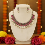 A pink and silver jewelry set consisting of a necklace and matching earrings, displayed on a clear plastic bag over a blue floral fabric background.