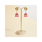A pair of traditional Indian jhumka earrings with pink beaded fringe and gold-tone hooks, displayed on a white card against a solid gray background.