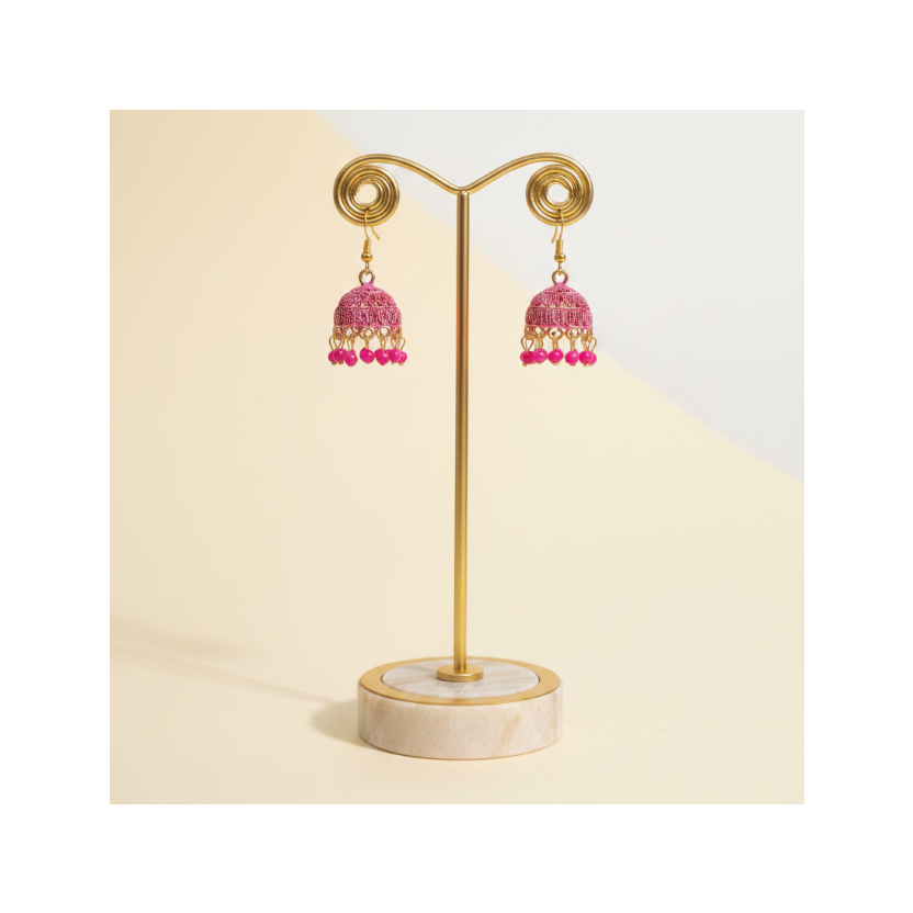 A pair of traditional Indian jhumka earrings with pink beaded fringe and gold-tone hooks, displayed on a white card against a solid gray background.
