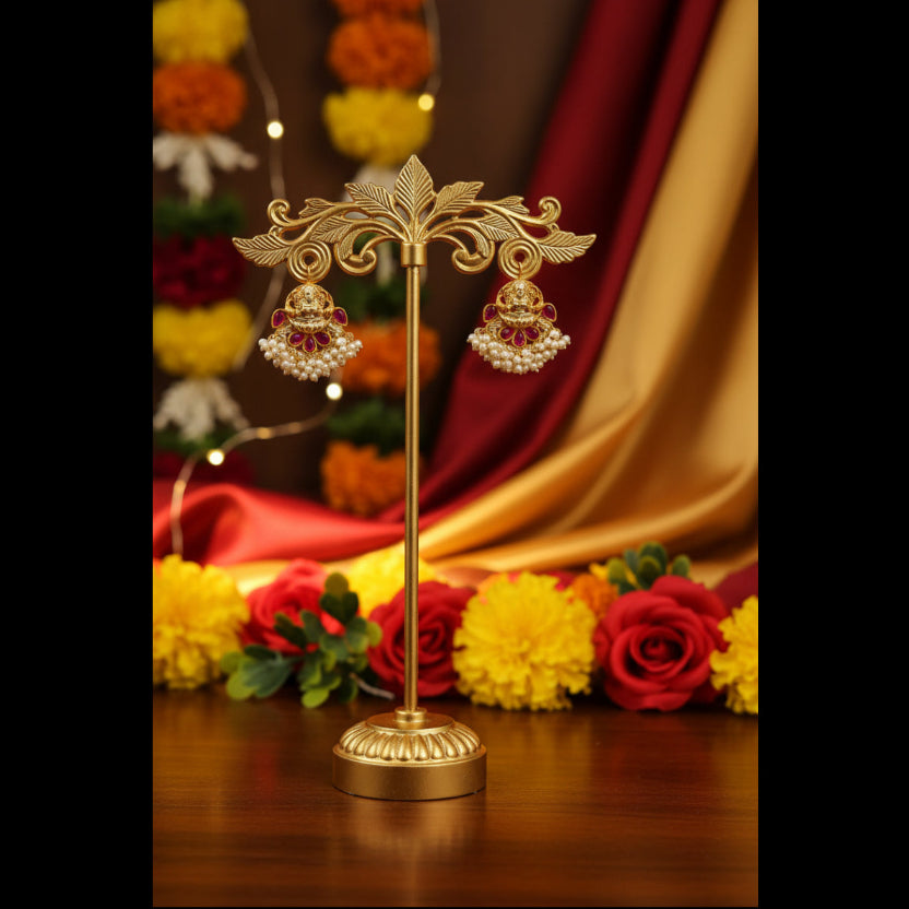 A pair of gold-toned traditional Indian earrings with red stone accents and white pearl-like bead borders, resting on a textured blue-gray fabric surface.