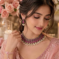 A woman wearing a pink embellished traditional outfit and jewelry set, featuring a pink and silver-toned beaded necklace with white pearl-like accents, matching drop earrings, and a bracelet.