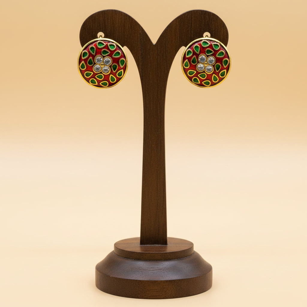 A pair of round gold-tone stud earrings with red enamel, green teardrop-shaped accents, and a central cluster of clear rhinestones, displayed on a textured white card.