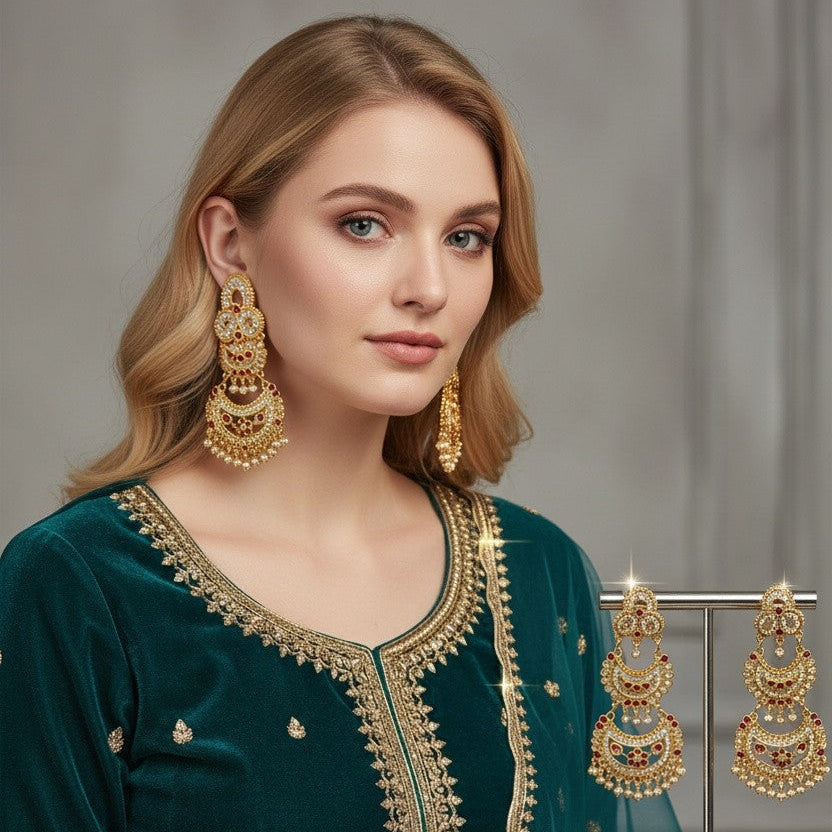 A woman wearing a deep teal green embroidered traditional outfit with gold detailing, styled with large gold earrings, against a soft gray studio background.
