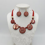 A red and cream beaded jewelry set featuring a beaded necklace and matching earrings with circular designs, laid out on a white faux fur background.