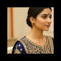 A woman in profile wearing a navy blue traditional outfit with ornate gold embroidery and a matching gold earring, photographed indoors against a softly blurred beige background.