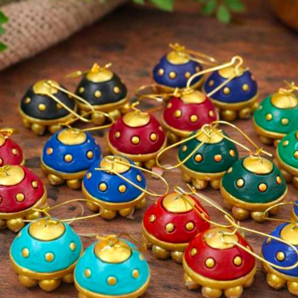 A group of small decorative terracotta-style ornaments or pendants with gold-tone tops and loops, shown in multiple colors including blue, red, green, teal, and black, arranged on a wooden surface. The text 'Avighna Terracotta' appears at the bottom.