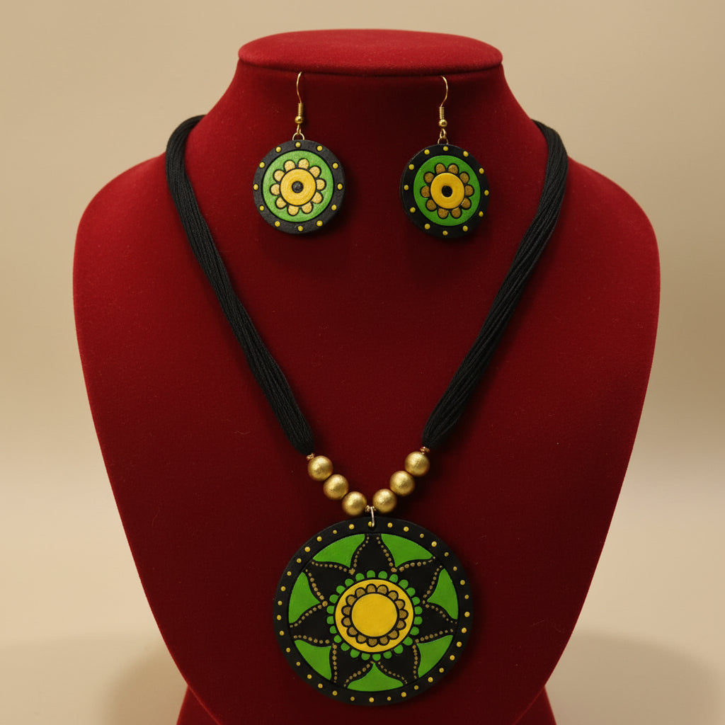 A handmade jewelry set featuring a black cord necklace and matching drop earrings with circular green, yellow, and black painted medallion pendants, displayed on a white mannequin bust.