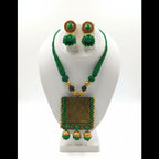 A green and gold jewelry set displayed on a white mannequin bust, featuring a necklace with a rectangular gold pendant, matching round earrings, and green beaded strands.