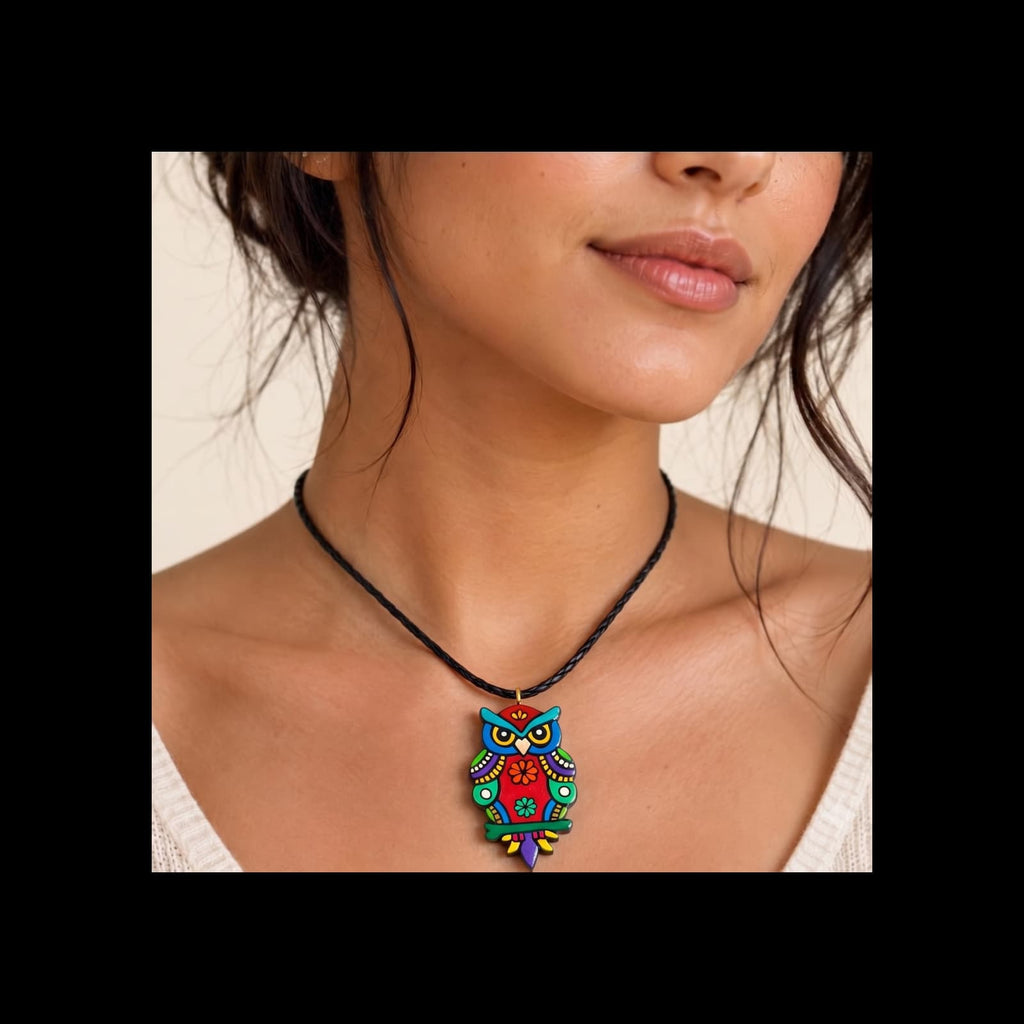 A close-up of a woman wearing a colorful owl pendant necklace on a black cord. The pendant features intricate hand-painted patterns in blue, red, green, yellow, and purple.
