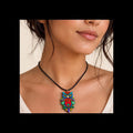 A close-up of a woman wearing a colorful owl pendant necklace on a black cord. The pendant features intricate hand-painted patterns in blue, red, green, yellow, and purple.
