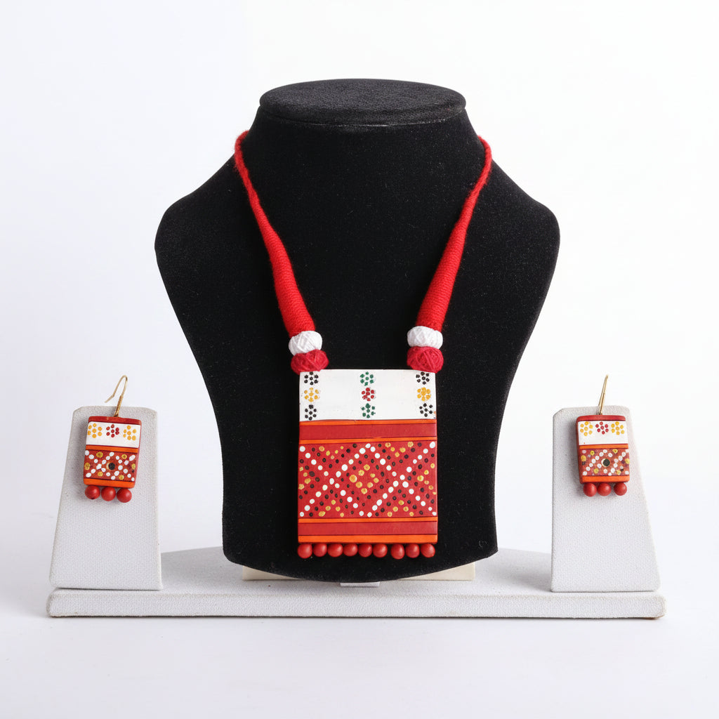 A traditional beaded necklace with a rectangular pendant and matching drop earrings, displayed on a black velvet jewelry bust. The necklace features a vibrant red braided cord and a white, red, and yellow geometric bead pattern.