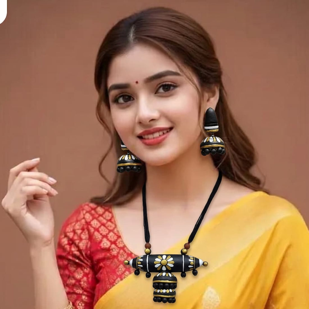 A woman wearing a black and gold traditional necklace with matching earrings, paired with a yellow and red saree, set against a solid brown background.