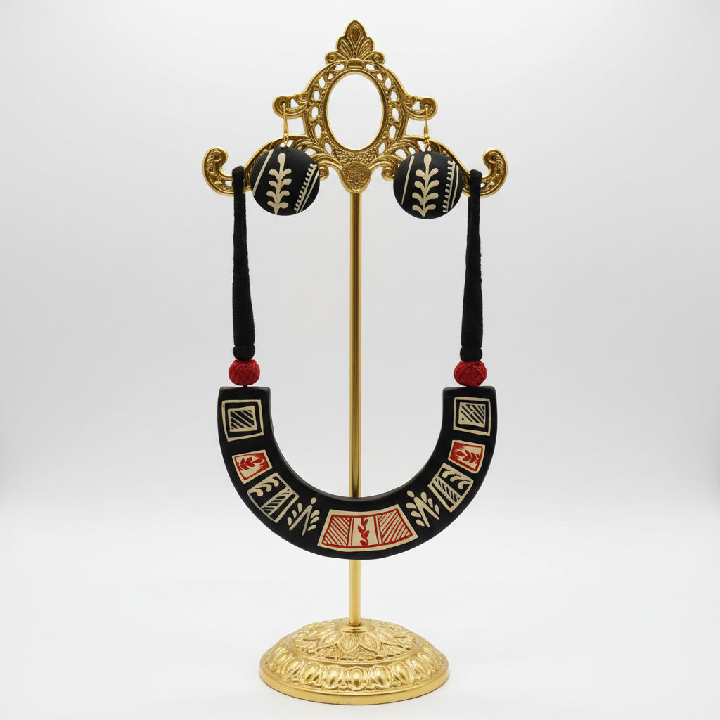 A handmade black wooden jewelry set featuring a U-shaped collar necklace and matching round drop earrings, displayed on a white card. The jewelry is decorated with hand-painted geometric and leaf-like patterns in beige and red, with black tassels and red beads.
