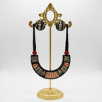 A handmade black wooden jewelry set featuring a U-shaped collar necklace and matching round drop earrings, displayed on a white card. The jewelry is decorated with hand-painted geometric and leaf-like patterns in beige and red, with black tassels and red beads.