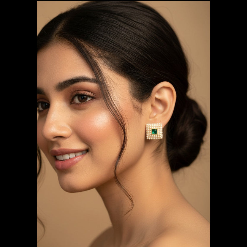 A close-up portrait of a woman wearing a square stud earring with a green center and a border of small clear stones, set against a warm beige background.