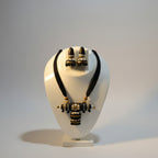 A black and gold clay jewelry set displayed on a white mannequin bust, featuring a necklace with a decorative pendant and matching earrings.