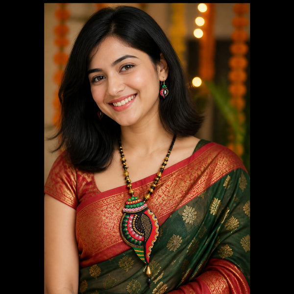 A woman wearing a traditional Indian saree with a deep green body, red border, and gold zari patterns, paired with a red and gold blouse. She is also wearing a large, colorful beaded statement necklace and matching earrings.