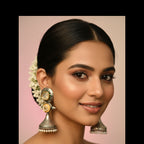 A pair of silver-toned jhumka earrings with gold and white stone accents, held in a person's hand.