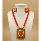 A decorative jewelry set featuring square gold-toned pendants and matching earrings with hand-painted floral motifs in orange, white, and red, accented with red tassels and gold beads, shown on a dark textured background.