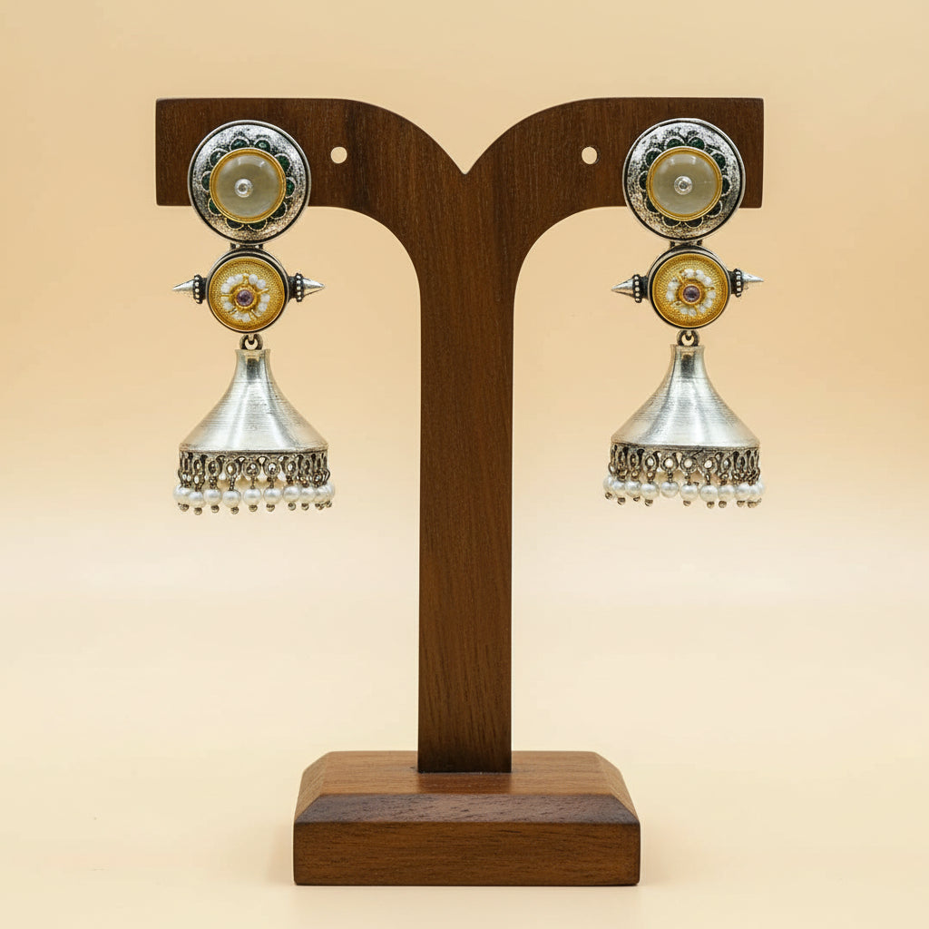A pair of silver-toned jhumka earrings with gold and white stone accents, held in a person's hand.